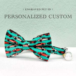 May include: A turquoise blue cat collar with a bow tie featuring a repeating pattern of red and white race cars. The collar has a silver bell charm with a white pearl.