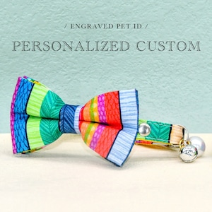 May include: A colorful, striped bow tie with a matching collar and bell for a cat. The collar is adjustable and has a safety release buckle. The bow tie is made of fabric and has a bright, cheerful pattern. The text "Personalized Custom" is visible at the top of the image.
