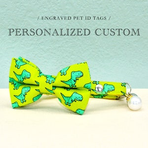 May include: A green and yellow bow tie with a dinosaur pattern and a matching collar with a bell. The collar has a silver clasp and a white pearl bell.