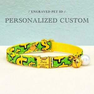 May include: A yellow and green cat collar with a gold buckle and a gold charm with the text "Daisy 123-456-7890". The collar has a white pearl charm and a gold bell charm.