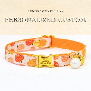 May include: Cat collar with an orange and white pumpkin print. The collar features a gold-coloured buckle engraved with a name and phone number. A gold bell and a white pearl charm are attached. The text "Engraved Pet ID" and "Personalized Custom" are at the top.