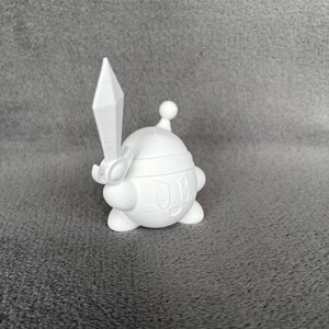 May include: A white 3D printed figurine of a pink character with a sword, wearing a helmet and holding a sword. The character has a round body and a smiling face.
