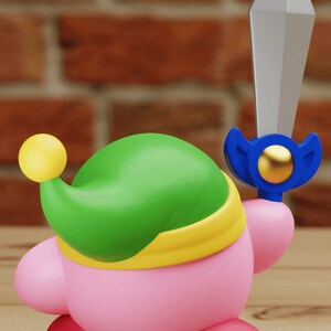 May include: A pink and green character with a yellow headband and a blue sword. The character is wearing a green hat with a yellow ball on top.