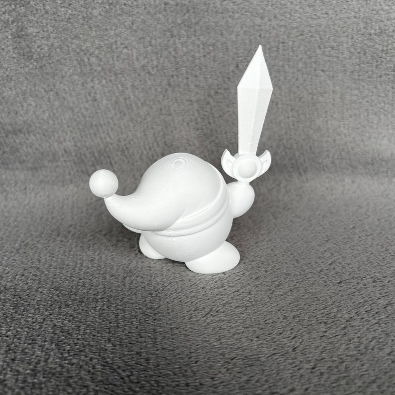 May include: White 3D printed figurine of a character holding a sword. The character is round and has a pointed hat.