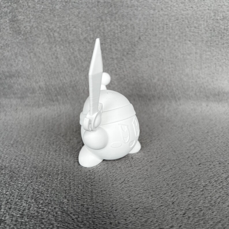 May include: White plastic figurine of a character holding a sword. The character has a round body and a small head with a single eye.