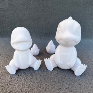May include: Two white, unpainted, plastic figurines of a Pokemon character. The figurines are sitting down with their legs spread out. The figurines are facing forward.