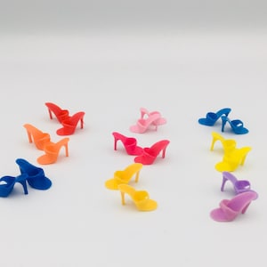 May include: A collection of miniature high-heeled mule sandals in various bright colors including red, orange, blue, pink, yellow, and purple. Each tiny shoe features a single strap across the toe and a slender stiletto heel, arranged in small groups.