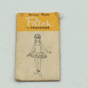 May include: A rectangular paper tag with a yellow top section featuring the text Nursery Rhyme Patch by PEDIGREE. The lower section is off-white and displays a black line drawing of a figure wearing a tutu and ballet slippers.