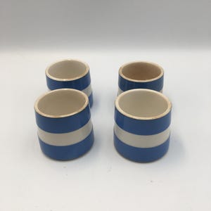 Può includere: Un set di quattro tazze cilindriche in ceramica caratterizzate da un motivo a righe orizzontali blu e bianche. Ogni tazza presenta un bordo arrotondato e liscio e una forma uniforme, con bande blu e bianche che avvolgono la superficie.