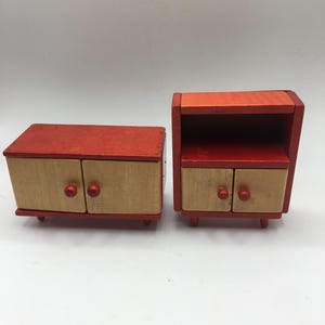 May include: Two miniature wooden furniture pieces. One is a low cabinet with two doors and red knobs. The other is a nightstand with a shelf and two drawers. Both are painted red and natural wood.