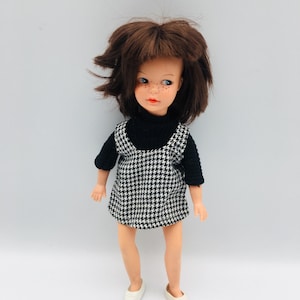 May include: A vintage doll with brown hair and freckles, wearing a black turtleneck sweater and a black and white houndstooth dress. The doll is also wearing white shoes. The doll is a collectible item.