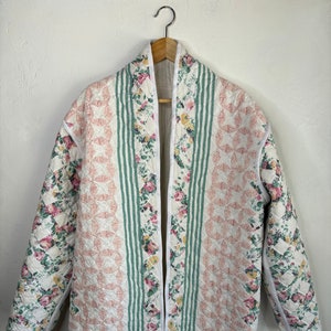 May include: A white quilted jacket with a floral print and green stripes. The jacket has a shawl collar and a long, open front.