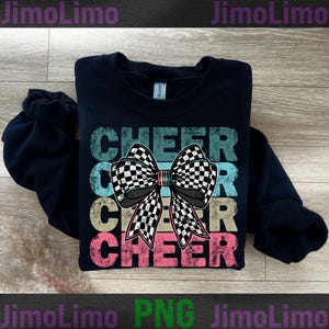 Op de afbeelding: Een zwart sweatshirt met een vintage-stijl grafisch ontwerp met het woord "CHEER" drie keer herhaald met een geruite strik in het midden. Het ontwerp is in tinten roze, blauw en geel.