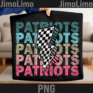 May include: Black tote bag featuring the word "PATRIOTS" in a stacked design with a checkered lightning bolt graphic. The text is in various colors, including teal, beige, and pink. The bag is held by a person.