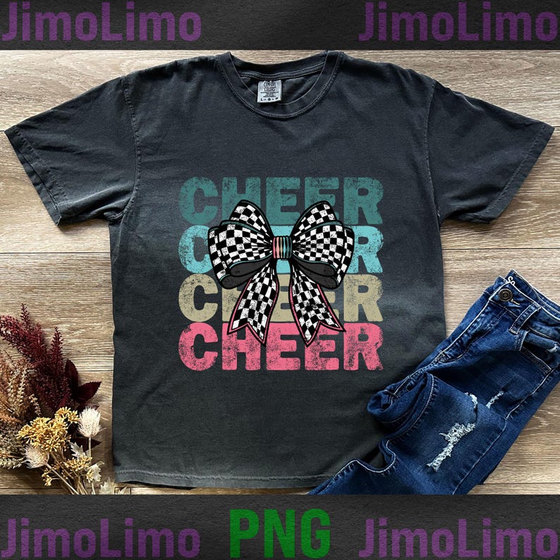 Op de afbeelding: Een zwart T-shirt met een vintage ontwerp met het woord "CHEER" drie keer herhaald in verschillende kleuren. Een geruite strik bevindt zich in het midden van het shirt.