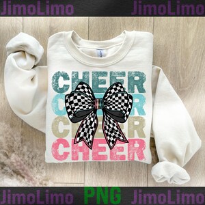Op de afbeelding: Een wit sweatshirt met het woord "CHEER" bedrukt in een vintage stijl met een geruite strik in het midden. Het woord "CHEER" wordt drie keer herhaald in verschillende kleuren.