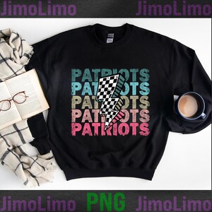 May include: Black sweatshirt with the word "PATRIOTS" stacked in a retro font, with a checkered lightning bolt graphic. The text is in shades of blue, tan, and pink. A cup of coffee, a book, and glasses are in the background.