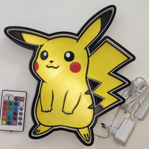 Puede incluir: Un letrero de neón Pikachu amarillo con contorno negro. El letrero se ilumina con una variedad de colores y viene con un control remoto para cambiar los colores. El letrero está conectado a una toma de corriente.