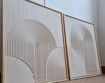 May include: Two abstract paintings with a white background and raised, textured lines forming geometric shapes. The paintings are framed in natural wood.