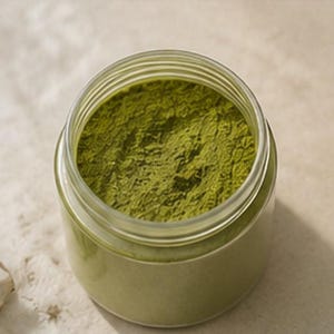 May include: A clear glass jar filled with finely ground, vibrant green powder. The jar has a wide opening and a screw-on lid. The powder appears to be a natural product, possibly a spice or herb, and is a rich, earthy green color.