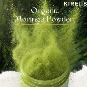 May include: A jar of organic moringa powder with a green hue, with powder being released into the air. The text "Organic Moringa Powder" is displayed in white, with the brand name "KIREIIS" in the top right corner.