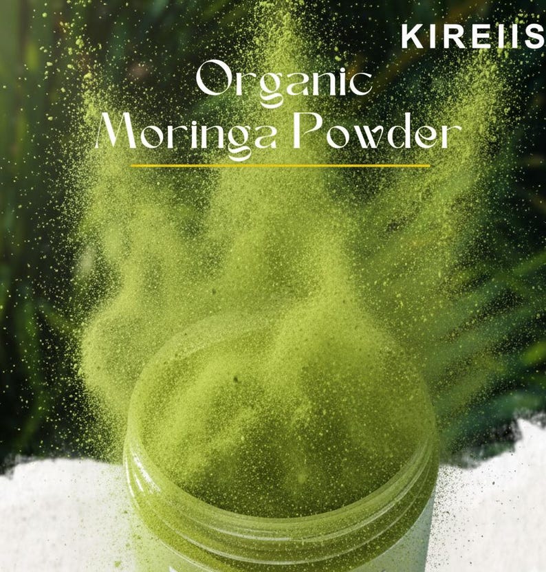 May include: A jar of organic moringa powder with a green hue, with powder being released into the air. The text "Organic Moringa Powder" is displayed in white, with the brand name "KIREIIS" in the top right corner.