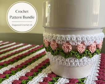May include: A white ceramic pot with a crocheted cover featuring pink flowers and green leaves. The pot is sitting on a crocheted placemat with a striped pattern of white, pink, and green.