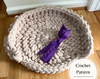 May include: A crocheted dog bed in a light beige colour with a purple toy in the shape of a flower. The text "Crochet Pattern" and "Dogwood Crochet US" is visible in the image.