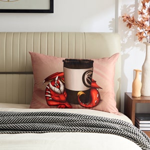 May include: A pink pillow with a red dragon curled around a coffee cup. The dragon has a white underbelly and a black nose. The coffee cup has a white band around it with a black logo.