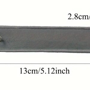 K&ouml;nnte beinhalten: Ein grauer Stoffschl&uuml;sselanh&auml;nger mit einem silbernen Schl&uuml;sselring. Der Schl&uuml;sselanh&auml;nger ist 13 cm lang und 2,8 cm breit.