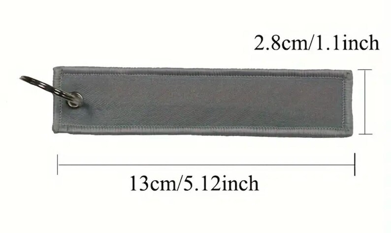 K&ouml;nnte beinhalten: Ein grauer Stoffschl&uuml;sselanh&auml;nger mit einem silbernen Schl&uuml;sselring. Der Schl&uuml;sselanh&auml;nger ist 13 cm lang und 2,8 cm breit.