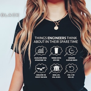 以下が含まれることがあります： 「Things Engineers Think About In Their Spare Time」という白い文字が書かれた黒いTシャツ。テキストは、それぞれ異なるアイコンとフレーズを含む9つの白い吹き出しで囲まれています。アイコンには、棒グラフ、コーヒーカップ、時計、天秤、3人の棒人間、更新矢印などがあります。