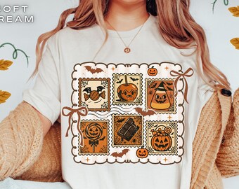 Pode incluir: Uma t-shirt de cor creme suave com uma impressão gráfica de seis ilustrações quadradas em estilo de selo postal. Os desenhos incluem um doce, uma maçã do amor, doce de milho, um pirulito, uma barra de chocolate e uma abóbora.