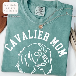 Peut inclure: T-shirt vert clair avec l'inscription blanche "CAVALIER MOM" et un dessin blanc d'un chien Cavalier King Charles Spaniel. Le t-shirt a un col rond et des manches courtes. Le texte "Multiple Colors Available" et "LIGHT GREEN" sont dans le coin sup&eacute;rieur gauche.