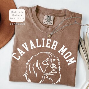 Peut inclure: T-shirt couleur expresso avec l'inscription "CAVALIER MOM" et un contour blanc d'un chien Cavalier King Charles Spaniel. Le t-shirt a un col rond et des manches courtes. Les mots "Multiple Colors Available" et "Espresso" sont dans un encadr&eacute; blanc.
