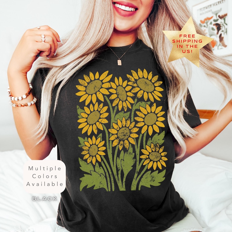May include: A black t-shirt with a vintage-style graphic of sunflowers in yellow and green. The text "Multiple Colors Available" and "BLACK" is printed on the shirt.