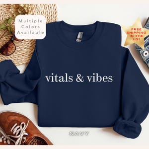May include: Navy blue sweatshirt with the text "vitals & vibes" in white lettering. The sweatshirt is a crew neck style.