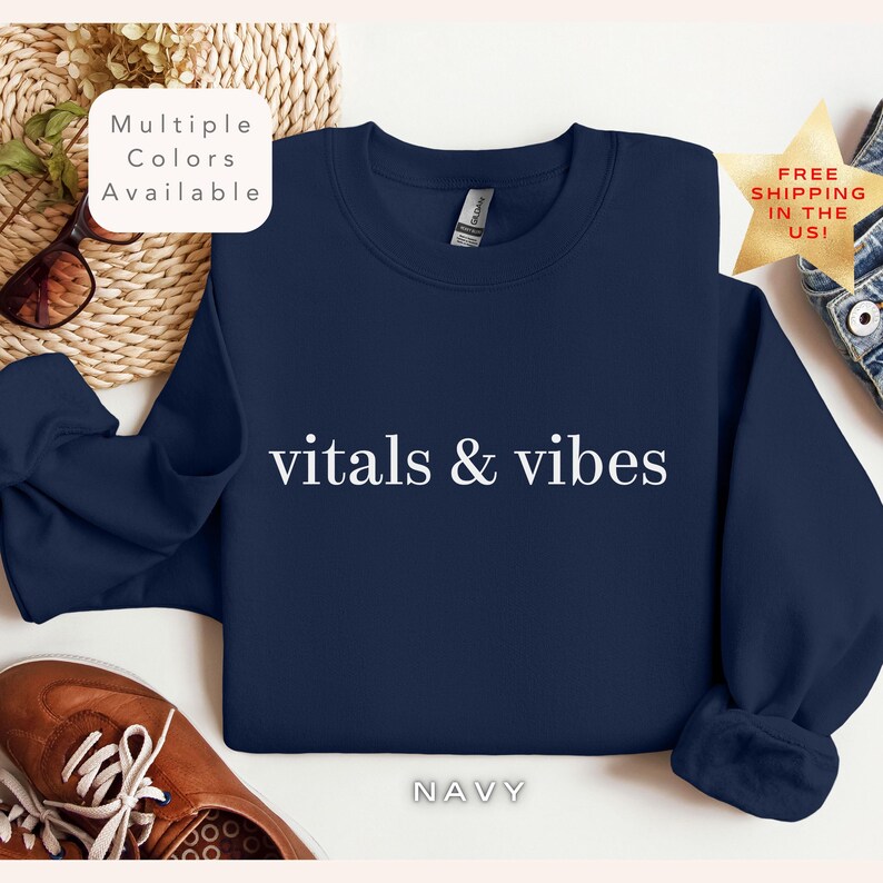 May include: Navy blue sweatshirt with the text "vitals & vibes" in white lettering. The sweatshirt is a crew neck style.