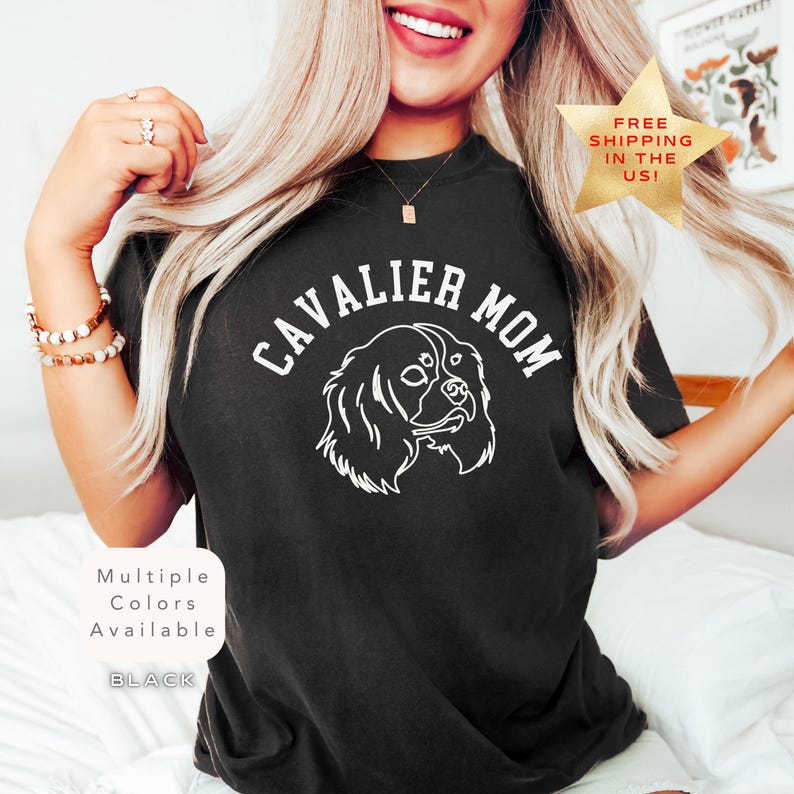 Peut inclure: T-shirt noir avec l'inscription blanche "CAVALIER MOM", orn&eacute;e d'une illustration de Cavalier King Charles Spaniel. Le t-shirt affiche &eacute;galement le texte "Multiple Colors Available" et "BLACK".
