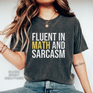 May include: A dark heather grey t-shirt with the text "Fluent in Math and Sarcasm" printed in white with the word "Math" in yellow.