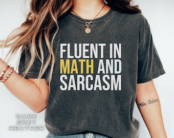 Puede incluir: Una camiseta gris jaspeado oscuro con el texto "Fluent in Math and Sarcasm" impreso en blanco, con la palabra "Math" en amarillo.