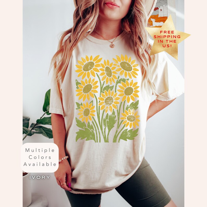 May include: A cream colored t-shirt with a vintage style sunflower print. The shirt has a relaxed fit and short sleeves. The text "Multiple Colors Available" and "IVORY" are visible on the image.
