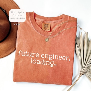 May include: A burnt orange t-shirt with the text "future engineer, loading..." in white. The shirt is made of a soft, comfortable material and has a relaxed fit.