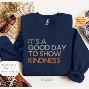 Puede incluir: Sudadera azul marino con el texto "It's a good day to show kindness" en un esquema de colores arcoíris.