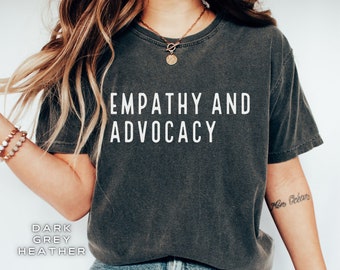 May include: A dark heather grey t-shirt with the text "EMPATHY AND ADVOCACY" printed in white on the front.