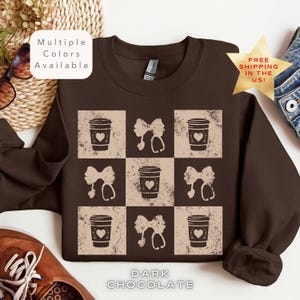 Könnte beinhalten: Ein braunes Sweatshirt mit einem abgenutzten Design, das abwechselnd Bilder einer Kaffeetasse mit einem Herzen und einem Stethoskop mit einer Schleife zeigt. Der Text "DARK CHOCOLATE" ist unter dem Design gedruckt.
