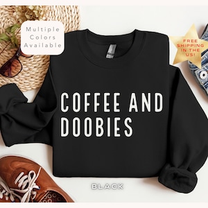May include: Black sweatshirt with the text "COFFEE AND DOOBIES" in white lettering. The sweatshirt is available in multiple colors.