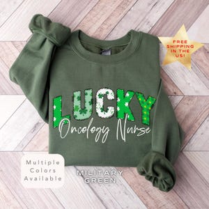 Może przedstawiać: Zielona bluza z napisem "LUCKY Oncology Nurse" w kolorze białym z wzorem koniczyny. Koniczyny są zielone, białe i żółte.