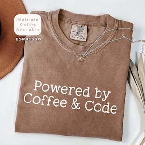 May include: A brown t-shirt with the text "Powered by Coffee & Code" in white. The shirt is made of a soft, comfortable material and has a distressed look.