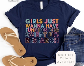 May include: Navy blue t-shirt with the text "GIRLS JUST WANNA HAVE FUNDING FOR SCIENTIFIC RESEARCH" in colorful block letters. The shirt is paired with denim shorts and sandals.